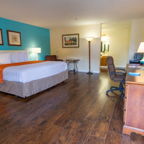 A spacious hotel room with a large bed, wooden furniture, a TV, a desk, and a vibrant blue accent wall.